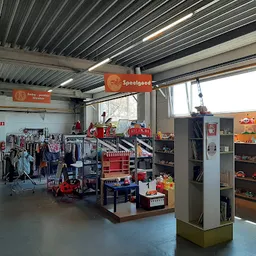 Winkelvloer met speelgoedrekken, displays en orange Sossigaad-signage onder golfplaten dak
