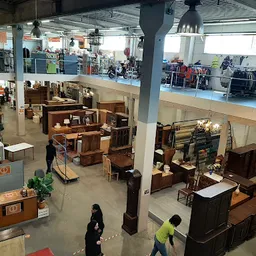 Ruim interieur van kringloopwinkel met meubels, kasten en huisraad uitgestald op de vloer en tegen de wanden