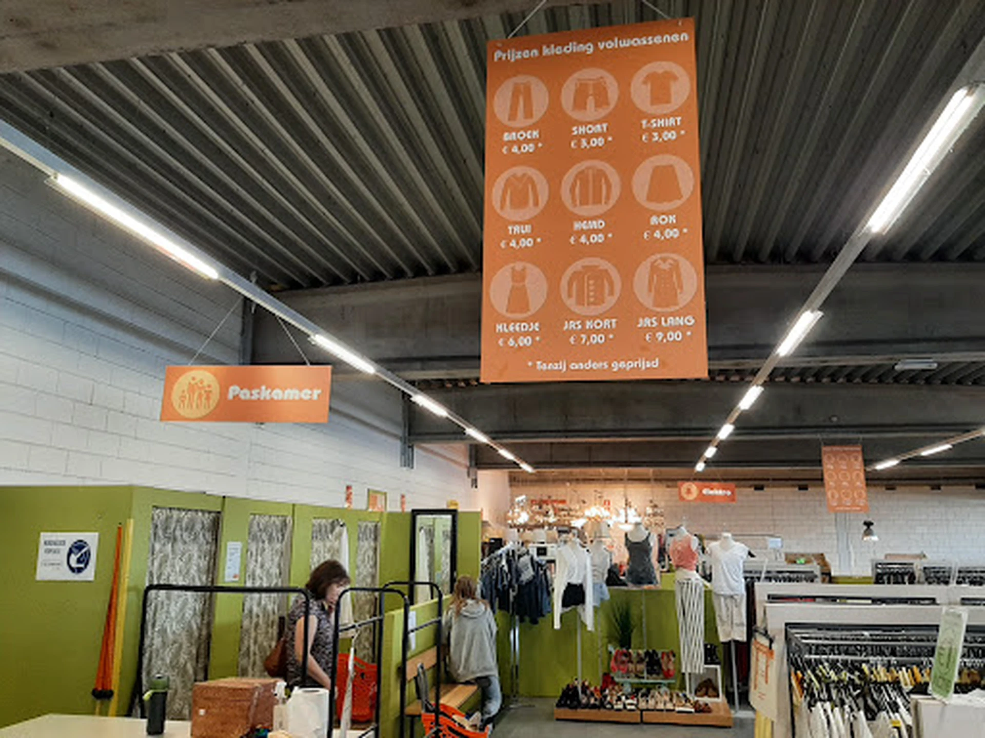 Magazijnachtig winkelinterieur met groene en witte muren, stellingen met kleding, fluorescente verlichting en hangrekken met 