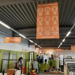 Magazijnachtig winkelinterieur met groene en witte muren, stellingen met kleding, fluorescente verlichting en hangrekken met 