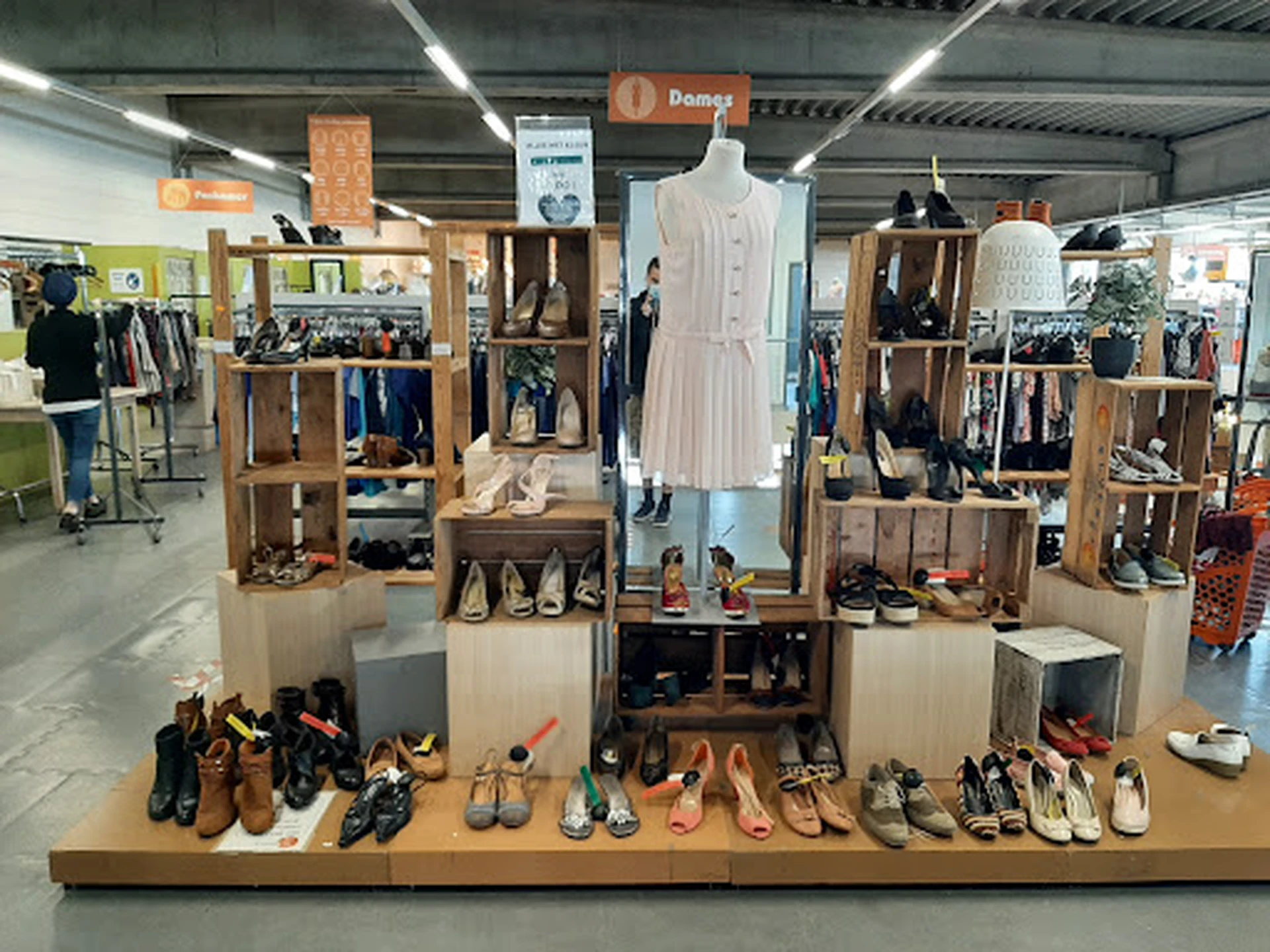 Uitgestalde schoenen, kleding en accessoires op houten stellingen met een mannequin in het midden