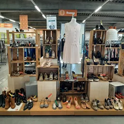 Uitgestalde schoenen, kleding en accessoires op houten stellingen met een mannequin in het midden