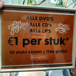 Oranje prijsbord met zwarte tekst: alle dvd's, cd's en lp's €1 per stuk, 10 stuks kopen = 1lde gratis