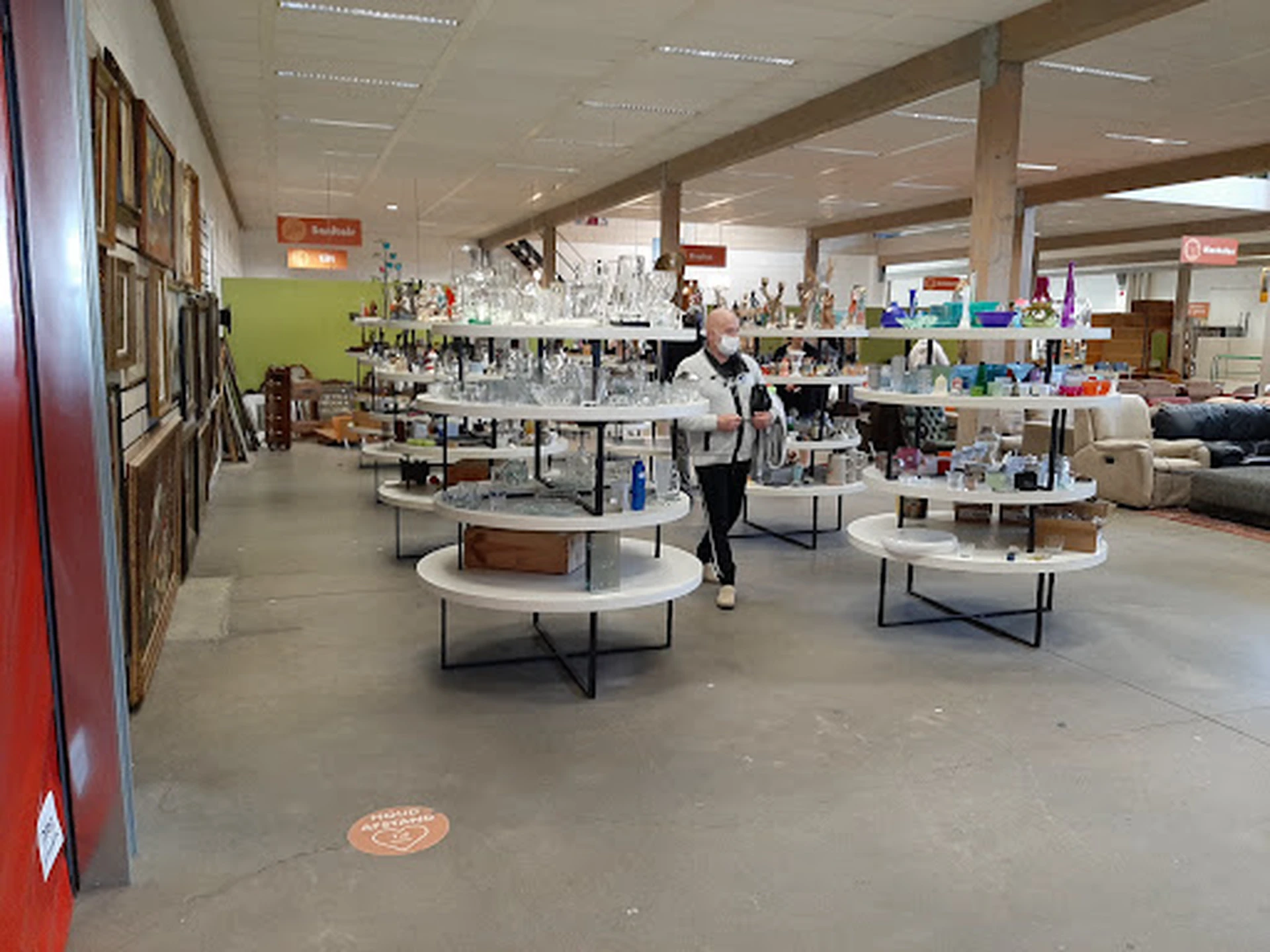 Ruim winkelinterieur met ronde tafels, stellingen met spullen en groene wand aan de zijkant
