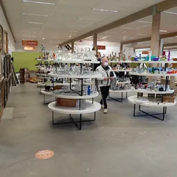 Ruim winkelinterieur met ronde tafels, stellingen met spullen en groene wand aan de zijkant