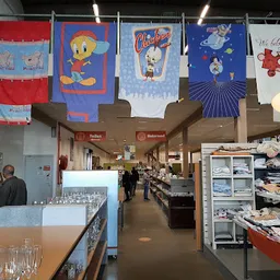 Binnenaanzicht van kringloopwinkel met gekleurde textiel aan touwen, rekken met tweedehandsartikelen en verlichte plafondlamp