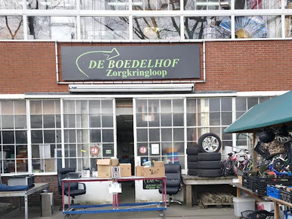 Gevel van kringloopwinkel met groot groen bord met winkelnaam, etalageruiten en daarachter zichtbare winkelinventaris