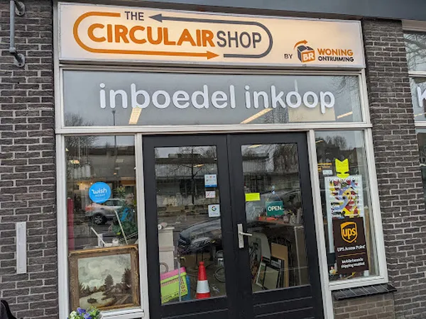 Gevel van The Circular Shop kringloopwinkel met donkergroene deuren en ramen, met bedrijfsnaam en 'inboedel inkoop' op gevel