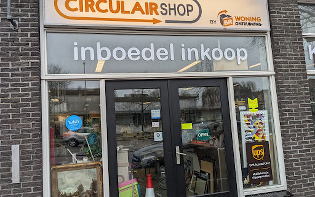 Gevel van The Circular Shop kringloopwinkel met donkergroene deuren en ramen, met bedrijfsnaam en 'inboedel inkoop' op gevel