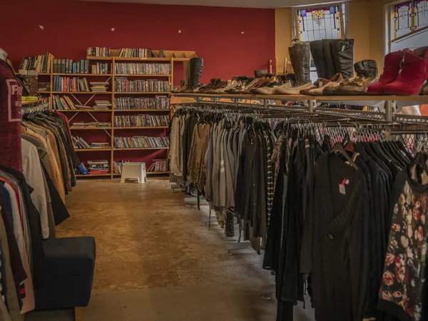 Interieur van kringloopwinkel met kledingrekken, boekenkasten en uitstallingen tegen rode en gele wanden