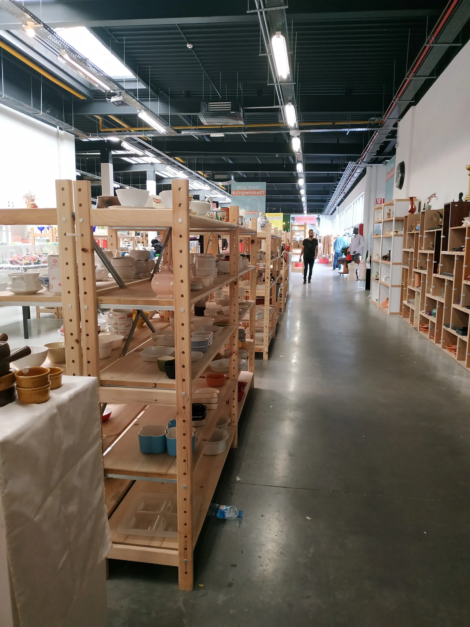 Winkelgang met houten stellingen en kasten vol tweedehands spullen in een ruime hal