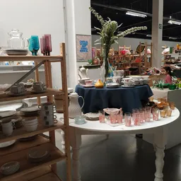 Uitgestalde tafelwaar, kandelaren en decoratieve items op ronde tafels in de winkel