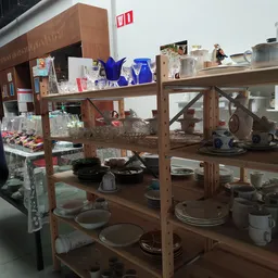 Houten stellingen met serviesgoed, glazen, kopjes en huishoudelijke artikelen.