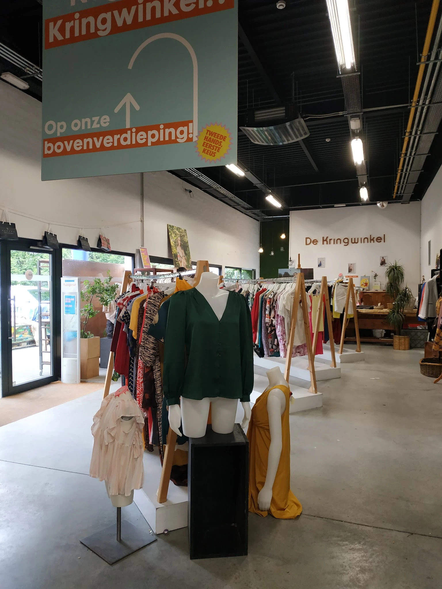 Winkelvloer met kledingrekken, mannequin met zwarte trui, en diverse tweedehands kleding aan houten hangers