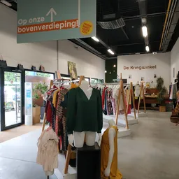 Winkelvloer met kledingrekken, mannequin met zwarte trui, en diverse tweedehands kleding aan houten hangers