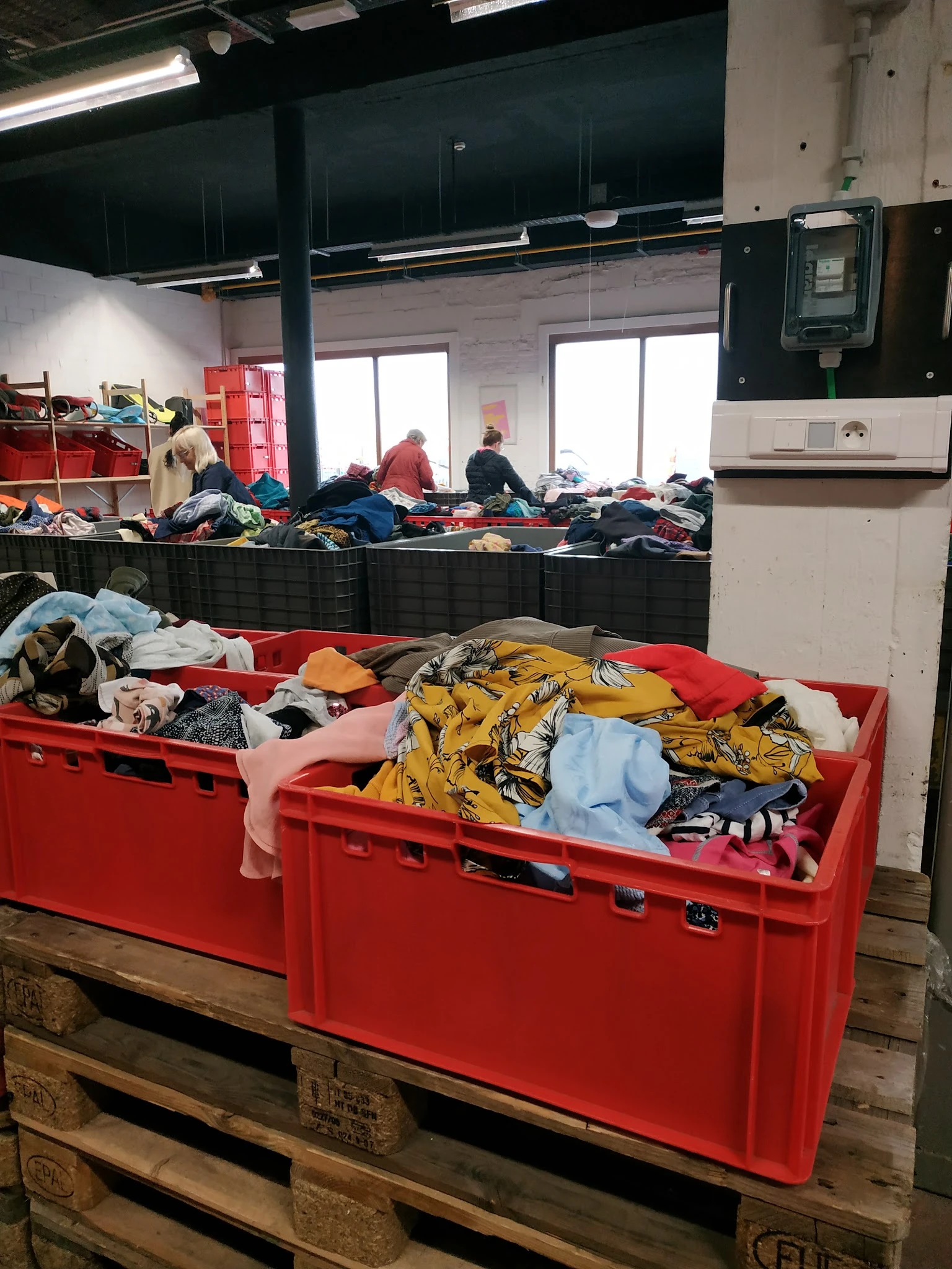 Rode plastic bakken vol met tweedehands kleding en textiel in de kringloopwinkel