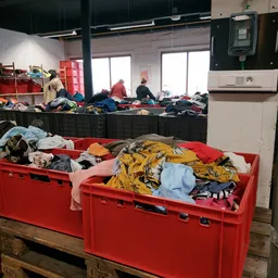 Rode plastic bakken vol met tweedehands kleding en textiel in de kringloopwinkel