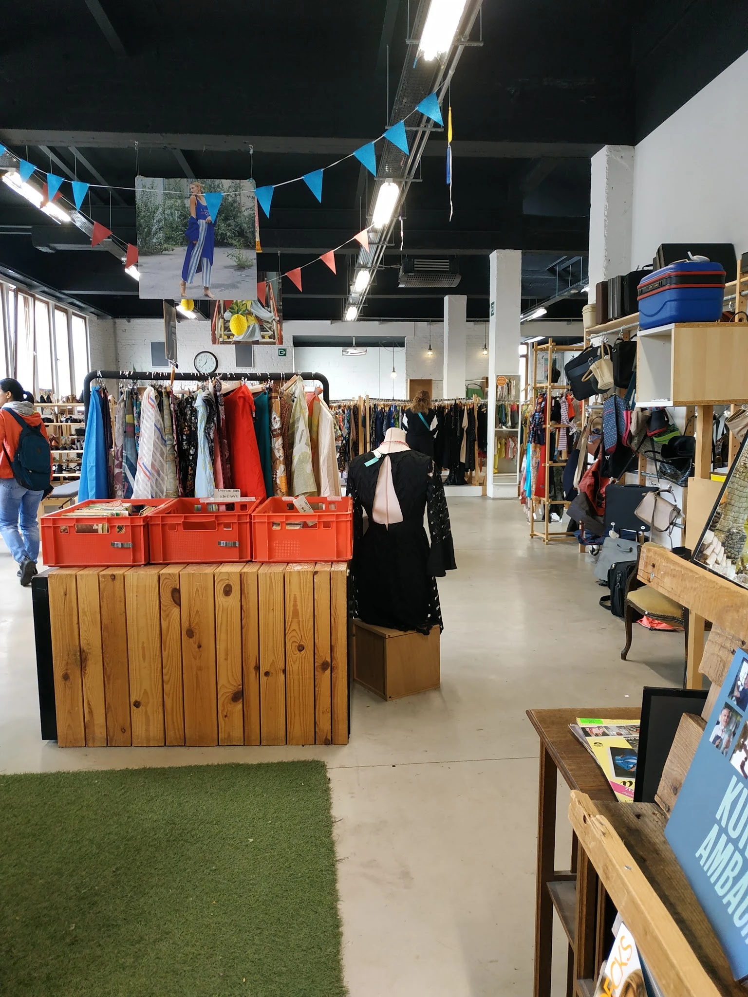 Winkelinterieur met kledingrekken, rode kisten en houten planken vol tweedehands artikelen