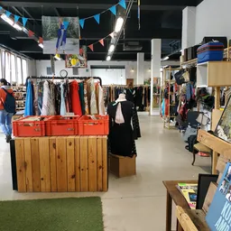 Winkelinterieur met kledingrekken, rode kisten en houten planken vol tweedehands artikelen