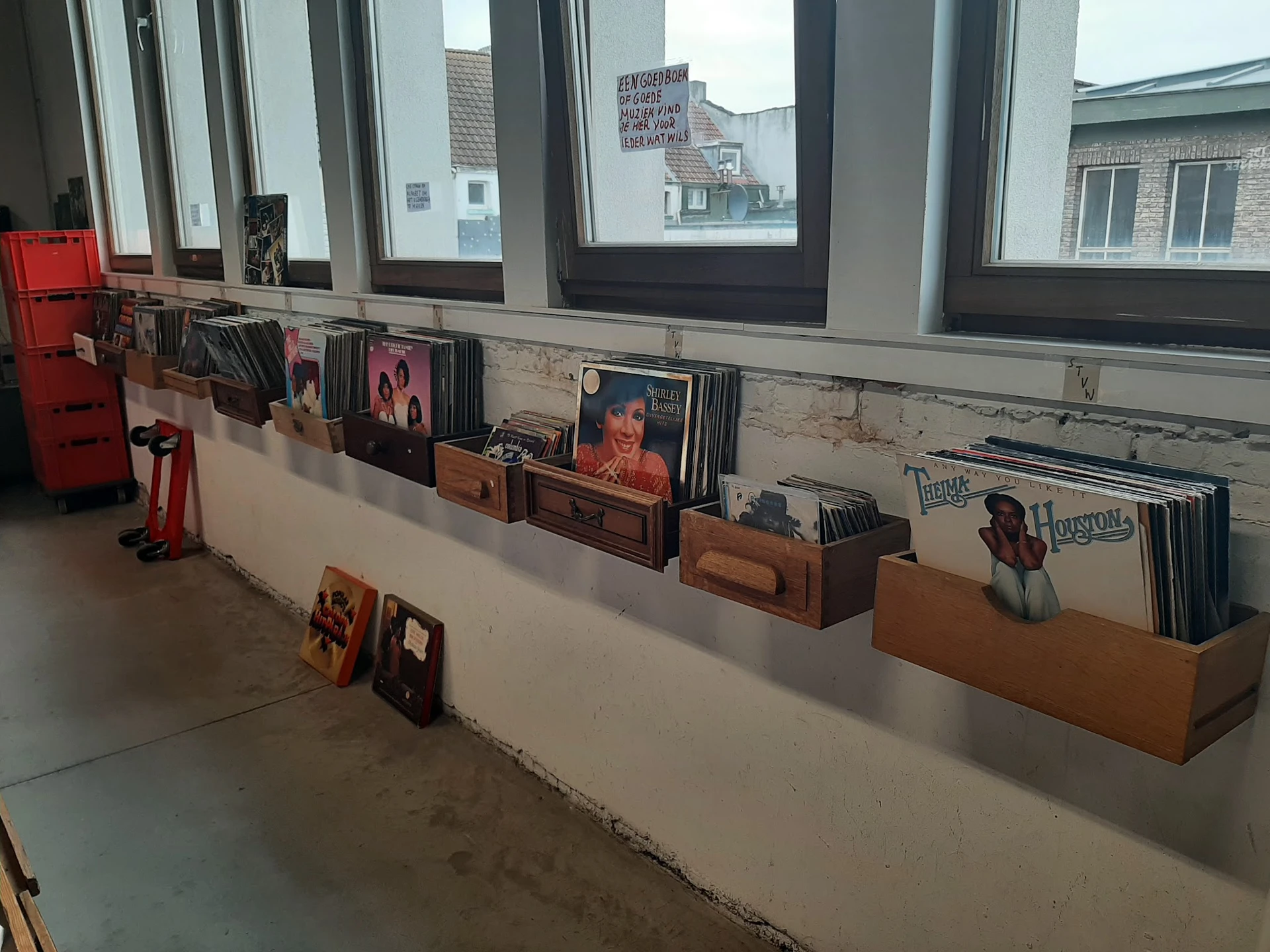 Uitgestalde cd's en vinyl records in bruine kartonnen bakken onder grote ramen