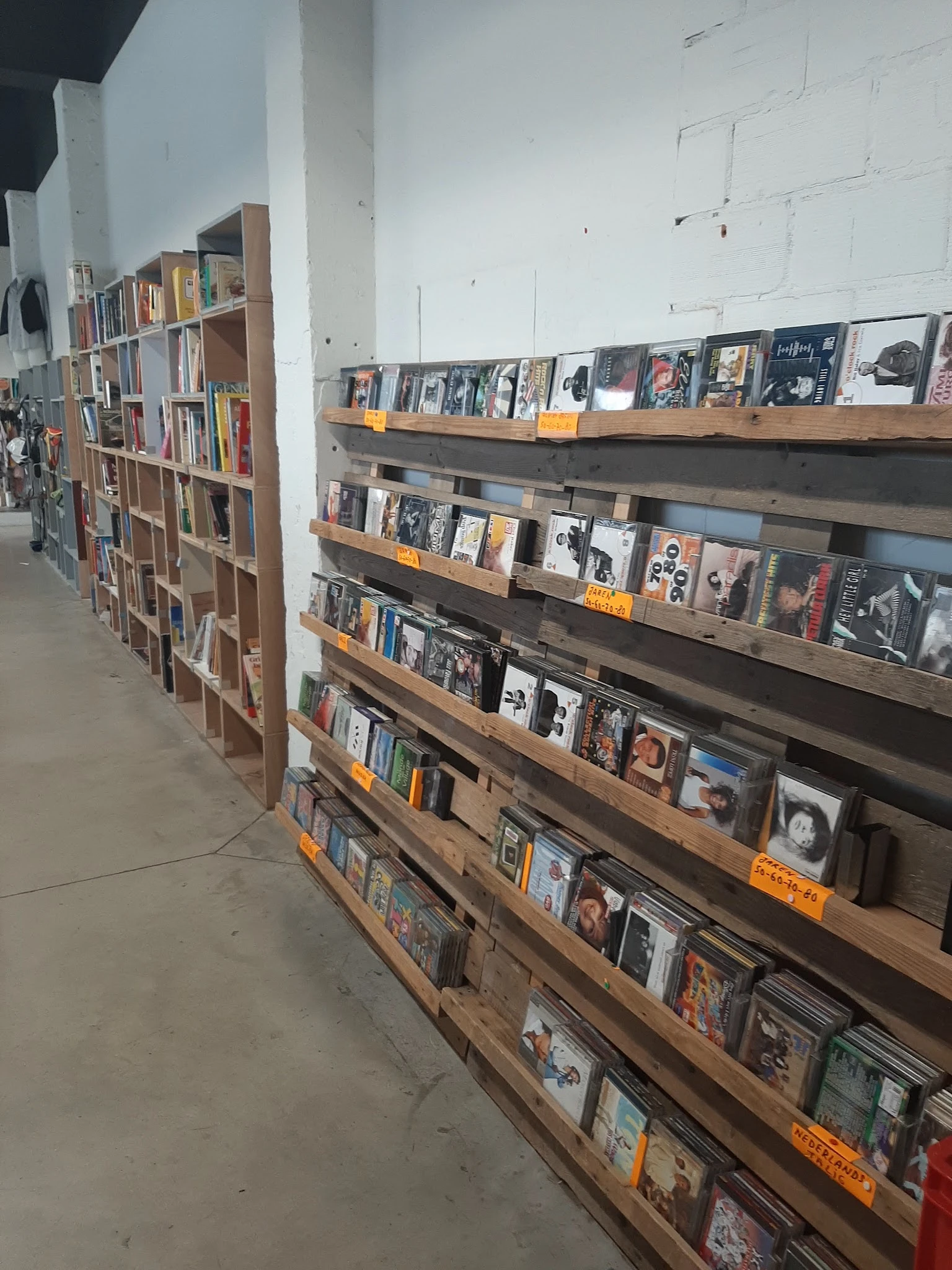 Houten stellingen met cd's, vinyl en dvd's uitgestald in rijen met gele prijskaartjes