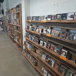 Houten stellingen met cd's, vinyl en dvd's uitgestald in rijen met gele prijskaartjes