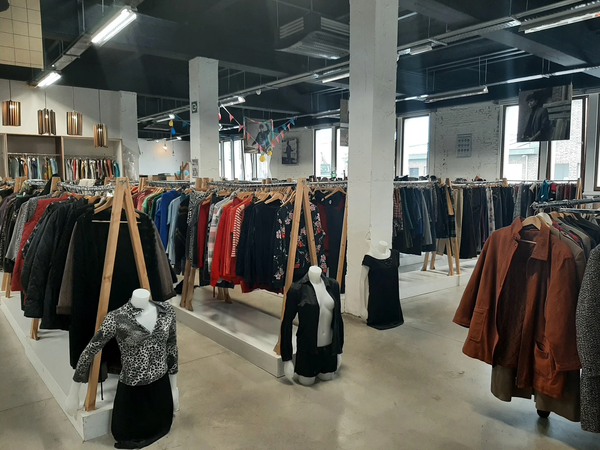 Ruim magazijnachtig interieur met houten kledingrekken vol tweedehands kleding op grijze betonvloer