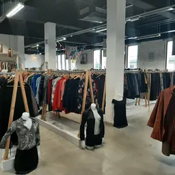 Ruim magazijnachtig interieur met houten kledingrekken vol tweedehands kleding op grijze betonvloer