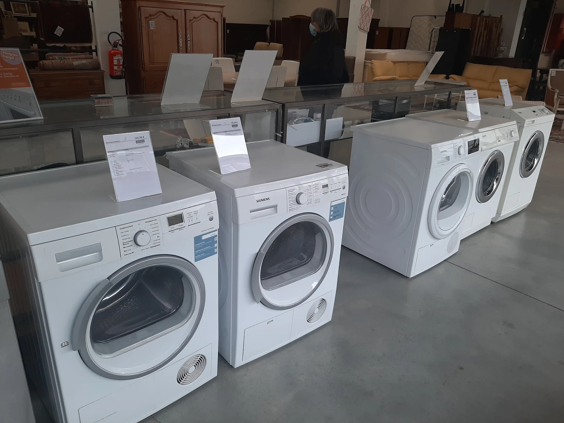 Vitrinekast met verschillende witte wasmachines en drogers met prijskaartjes