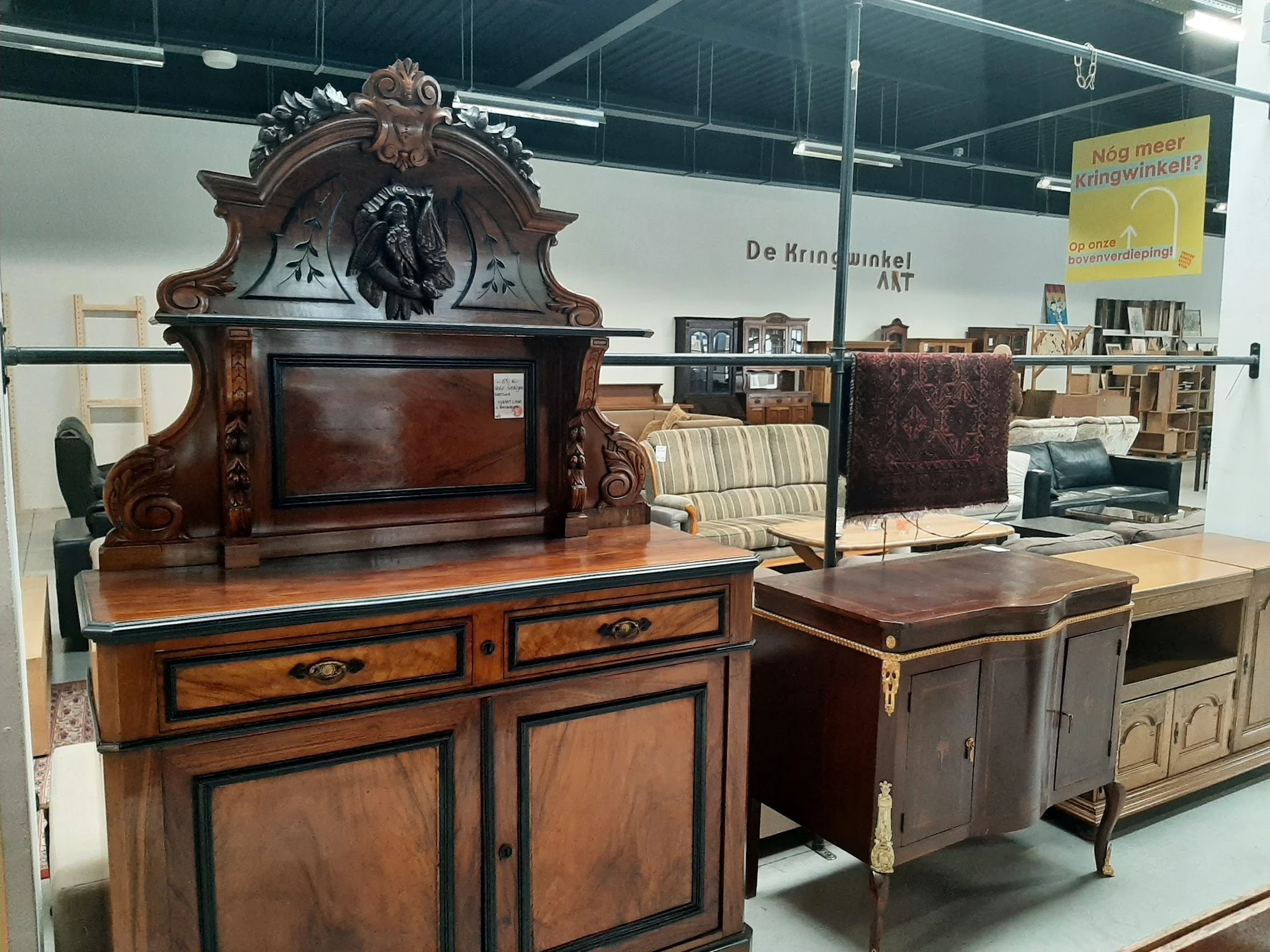 Antieke houten meubels uitgestald in de winkel, waaronder een imposante kast met ornamentale bovenkast en verschillende klein