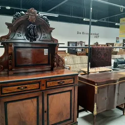 Antieke houten meubels uitgestald in de winkel, waaronder een imposante kast met ornamentale bovenkast en verschillende klein