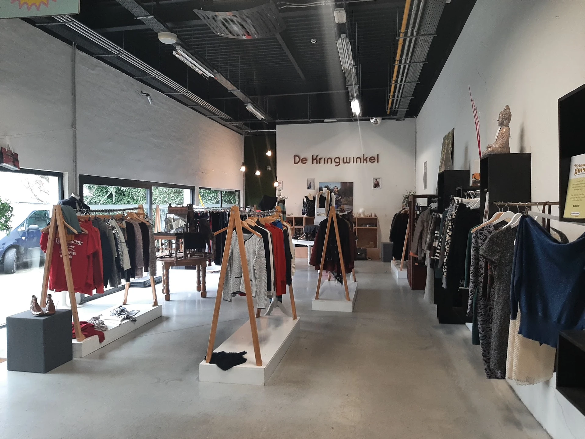 Winkelinterieur met kleding op houten rekken en stellingen, betonnen vloer en moderne verlichting