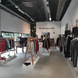 Winkelinterieur met kleding op houten rekken en stellingen, betonnen vloer en moderne verlichting