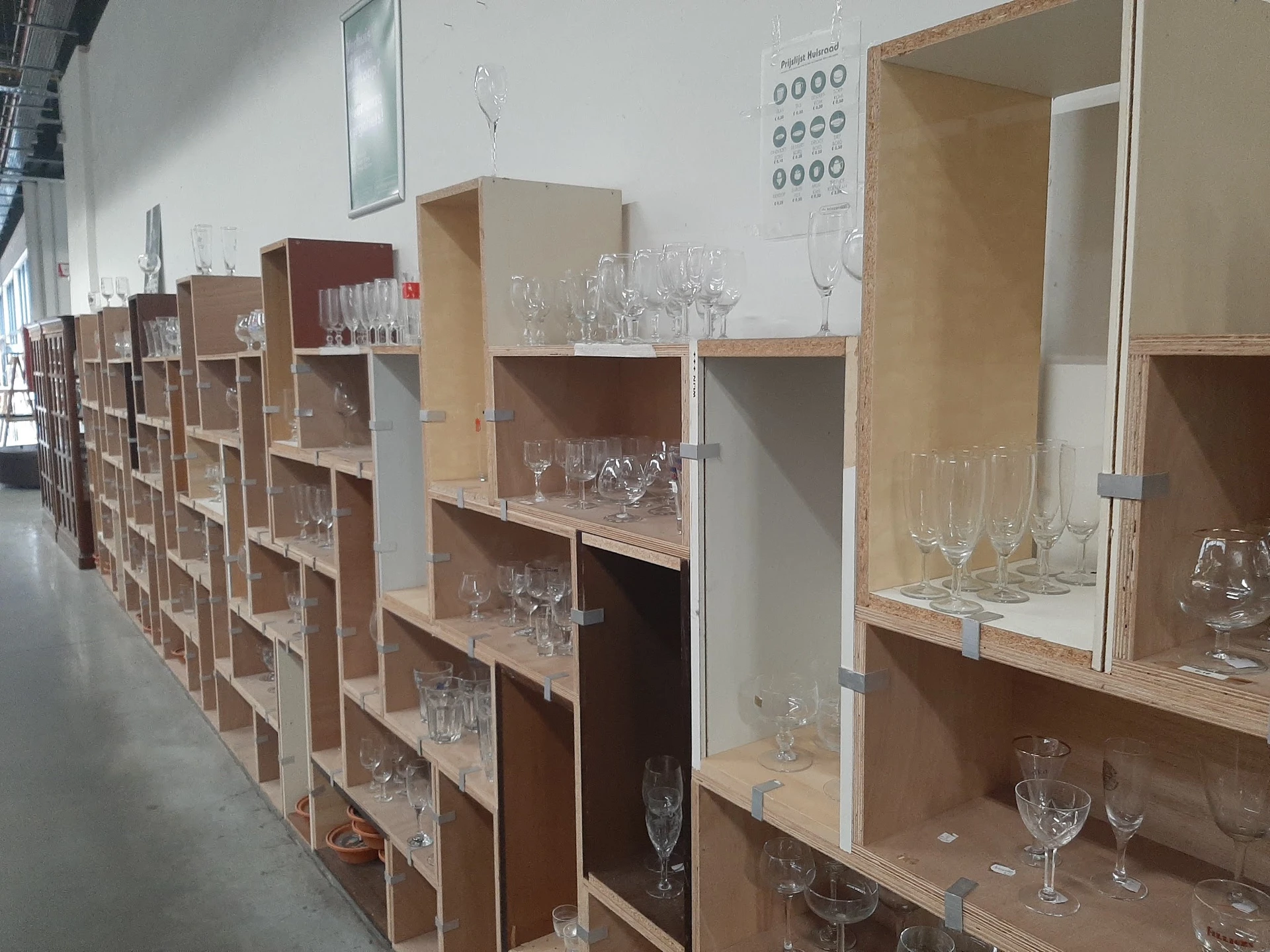 Houten stellingen met glazen bekers en drinkglazen uitgestald in verschillende vakken