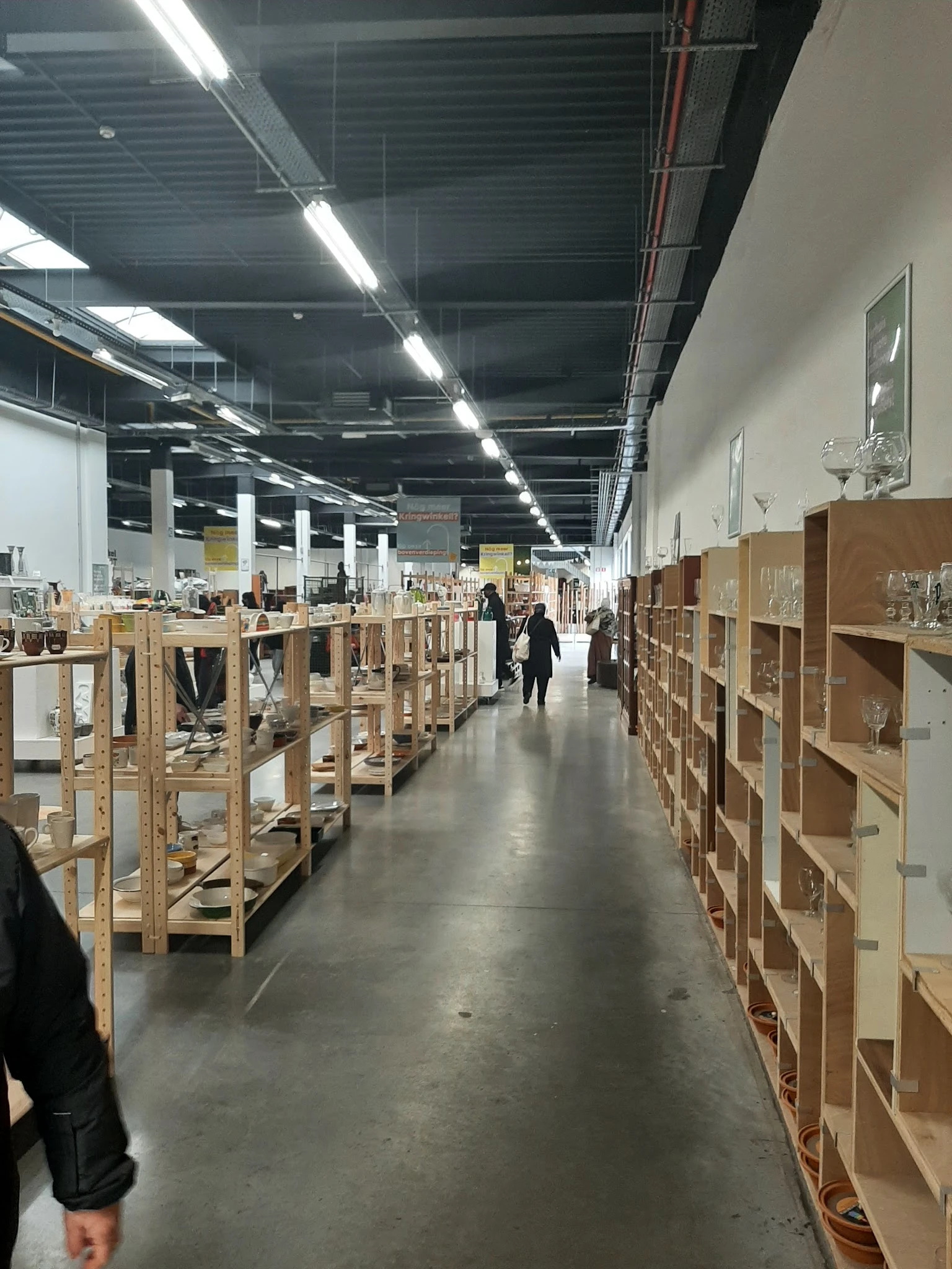 Winkelinterieur met houten stellingen en kasten vol spullen, bezoekers lopen tussen de gangen door