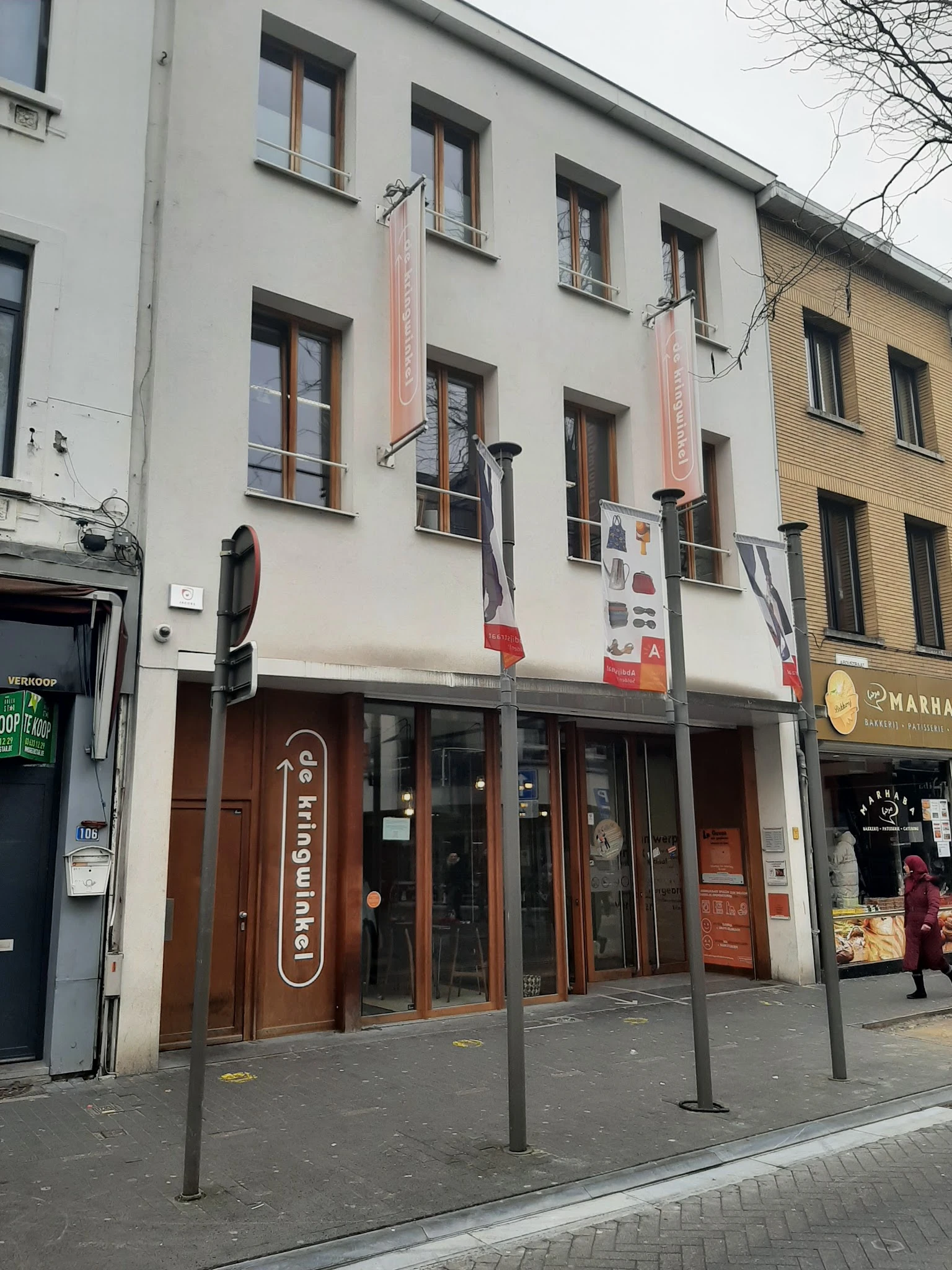 Gevel van een kringloopwinkel met bruine deuren, ramen en signage aan een straathoek