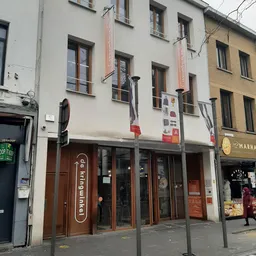 Gevel van een kringloopwinkel met bruine deuren, ramen en signage aan een straathoek