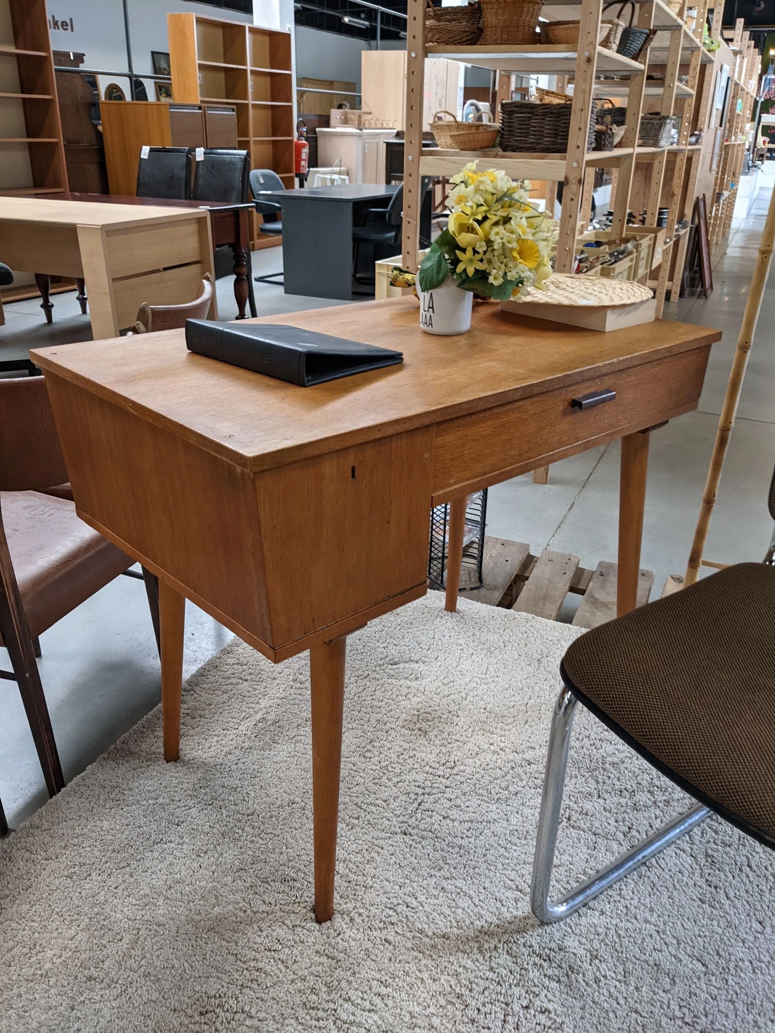 Houten bureau met lichtkleurig blad en lade, voorzien van decoratie, in een kringloopwinkel