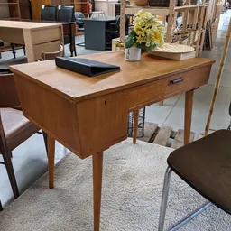 Houten bureau met lichtkleurig blad en lade, voorzien van decoratie, in een kringloopwinkel