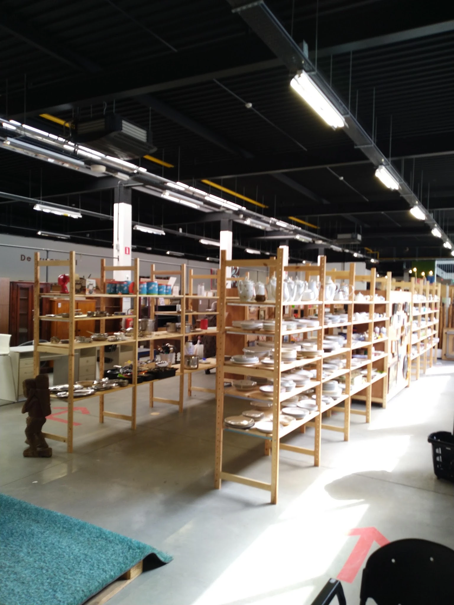 Ruim winkelinterieur met houten stellingen vol serviesgoed en huishoudarikelen onder fluorescerend licht