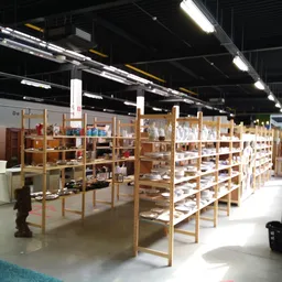 Ruim winkelinterieur met houten stellingen vol serviesgoed en huishoudarikelen onder fluorescerend licht