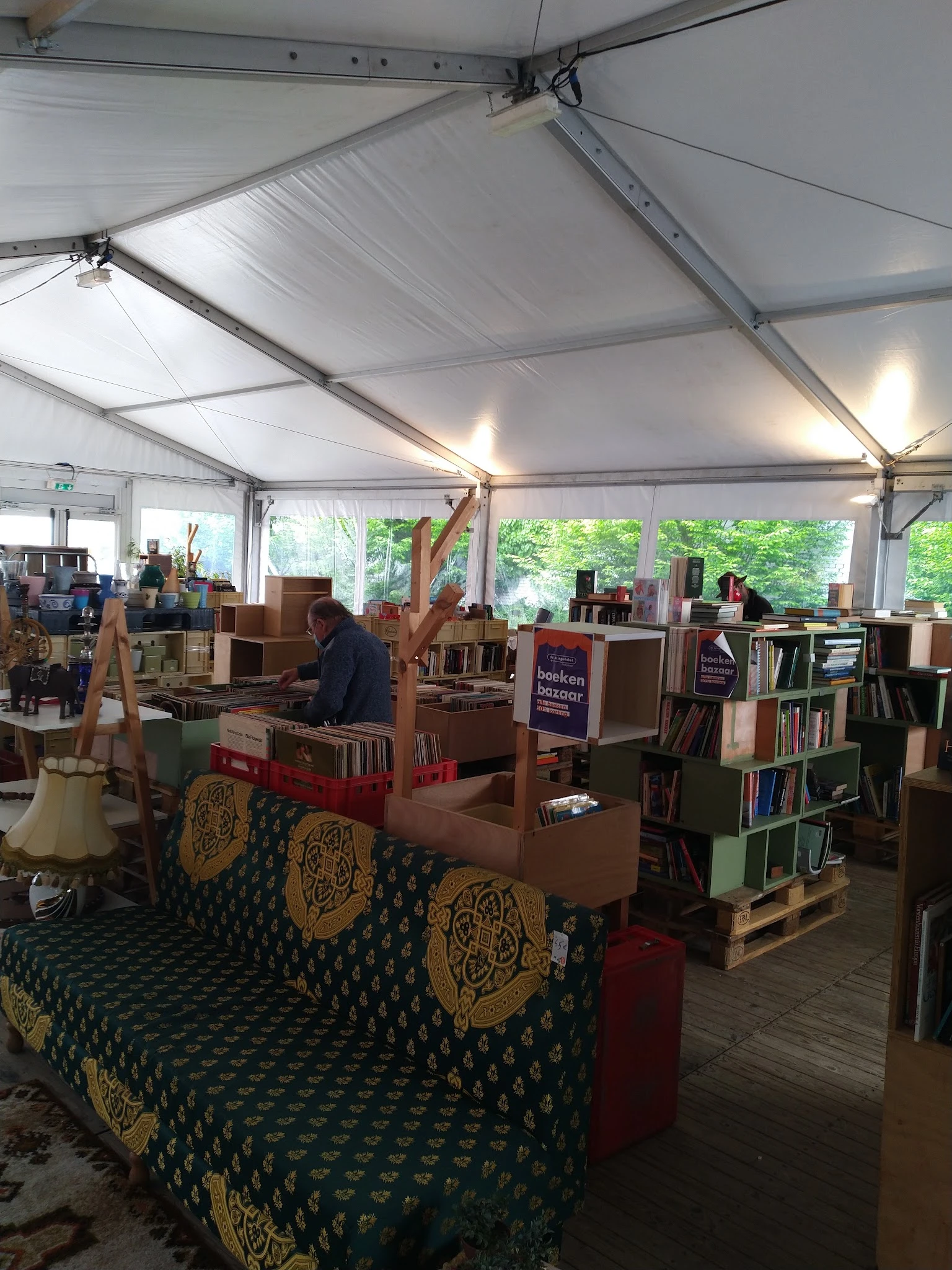 Ruim verlicht interieur van kringloopwinkel met boekenrekken, meubels en diverse spullen, groene vloer met patroon