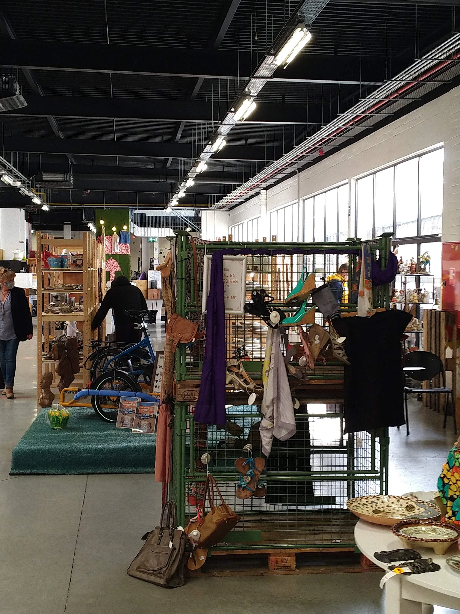 Winkelvloer van kringloopwinkel met diverse uitgestalde spullen, meubels, kleding en decoratie in verschillende standsecties