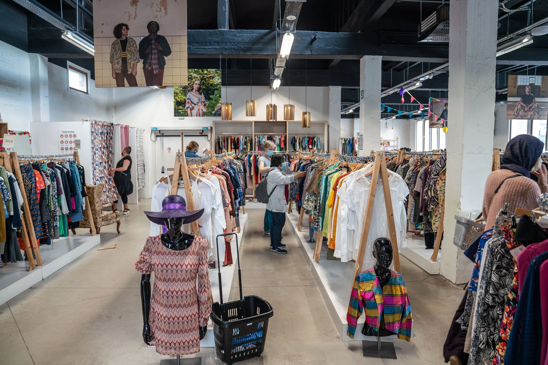 Ruime winkelhal met kledingrekken, mannequins in kleding en bezoekers die rondlopen tussen het aanbod