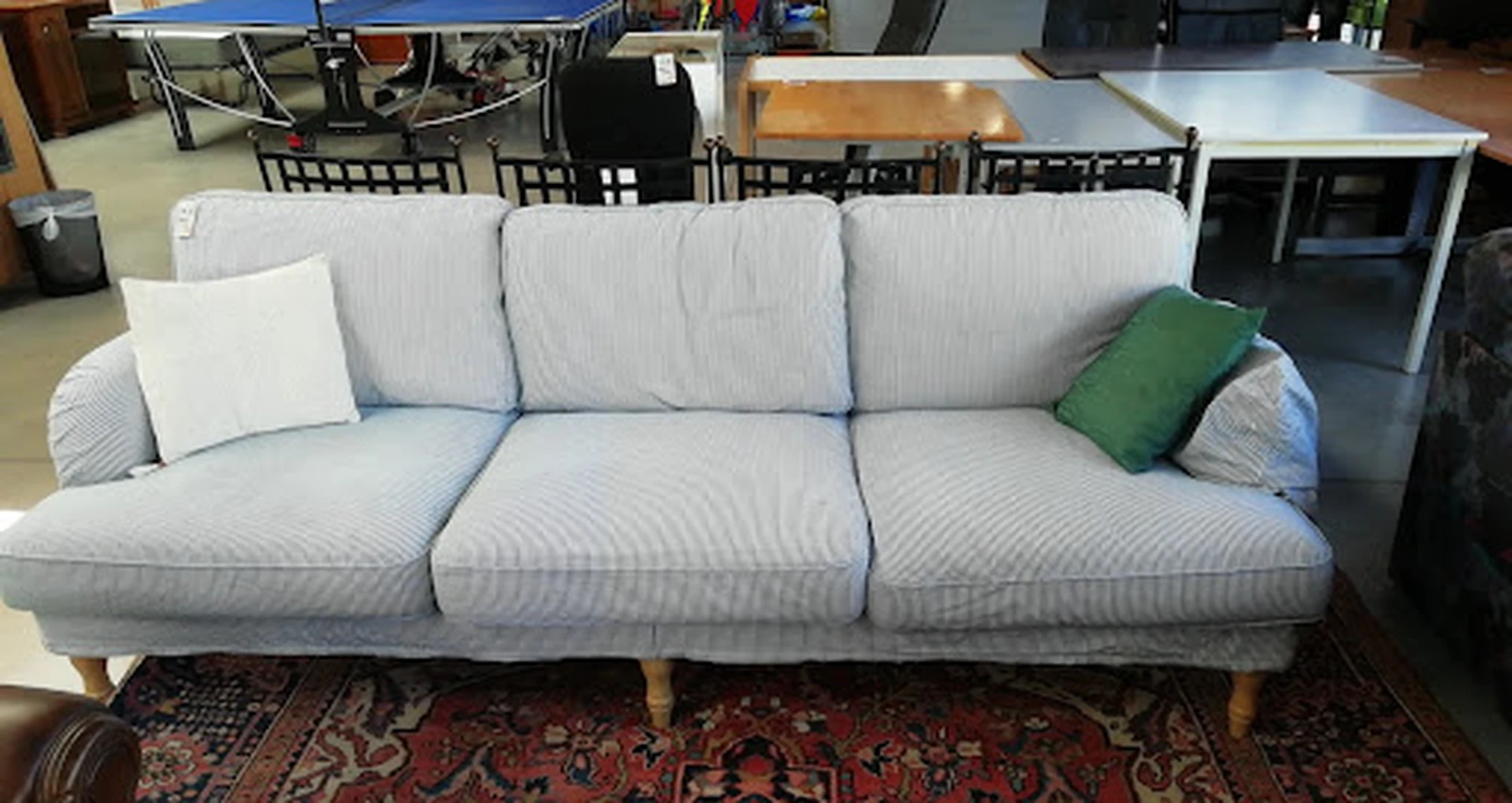 Lichtblauwe driezitsbank met houten poten en groene kussens op een oriental rug