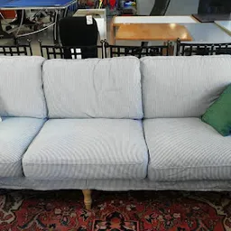 Lichtblauwe driezitsbank met houten poten en groene kussens op een oriental rug