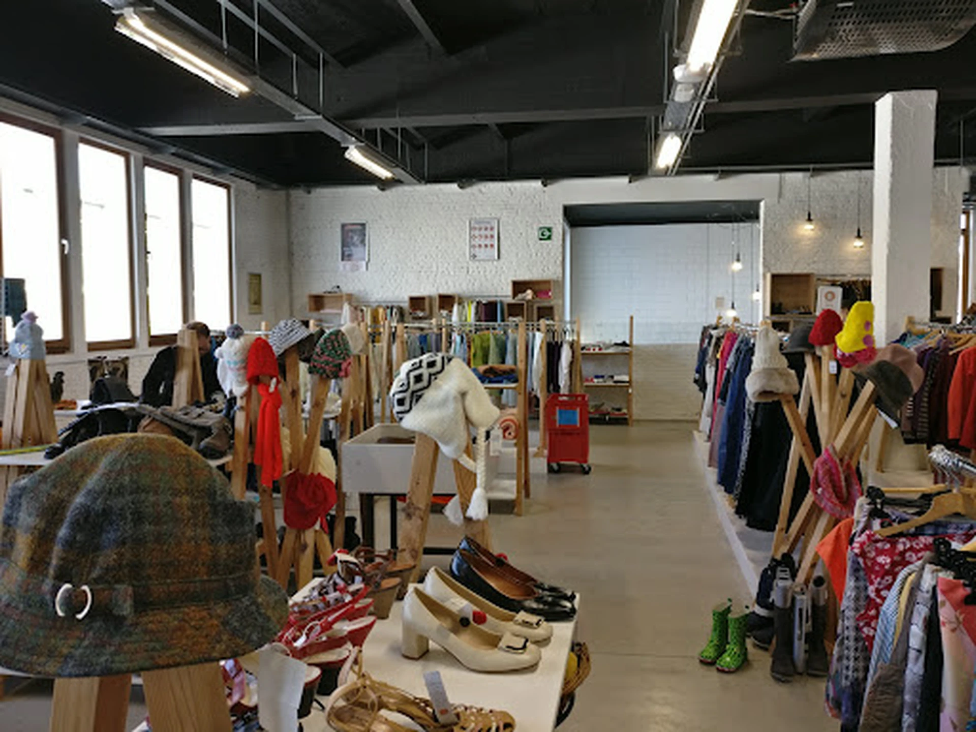 Ruime winkelhal met rekken vol tweedehands kleding, schoenen en accessoires, verlicht met industriële verlichting