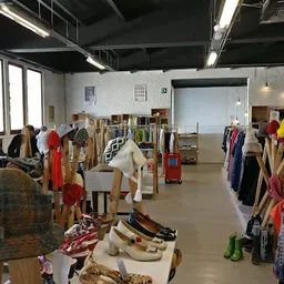 Ruime winkelhal met rekken vol tweedehands kleding, schoenen en accessoires, verlicht met industriële verlichting