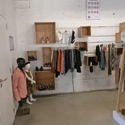 Winkelvloer van kringloopwinkel met houten stellingen, uitgestalde kleding op hangers en kledingrekken