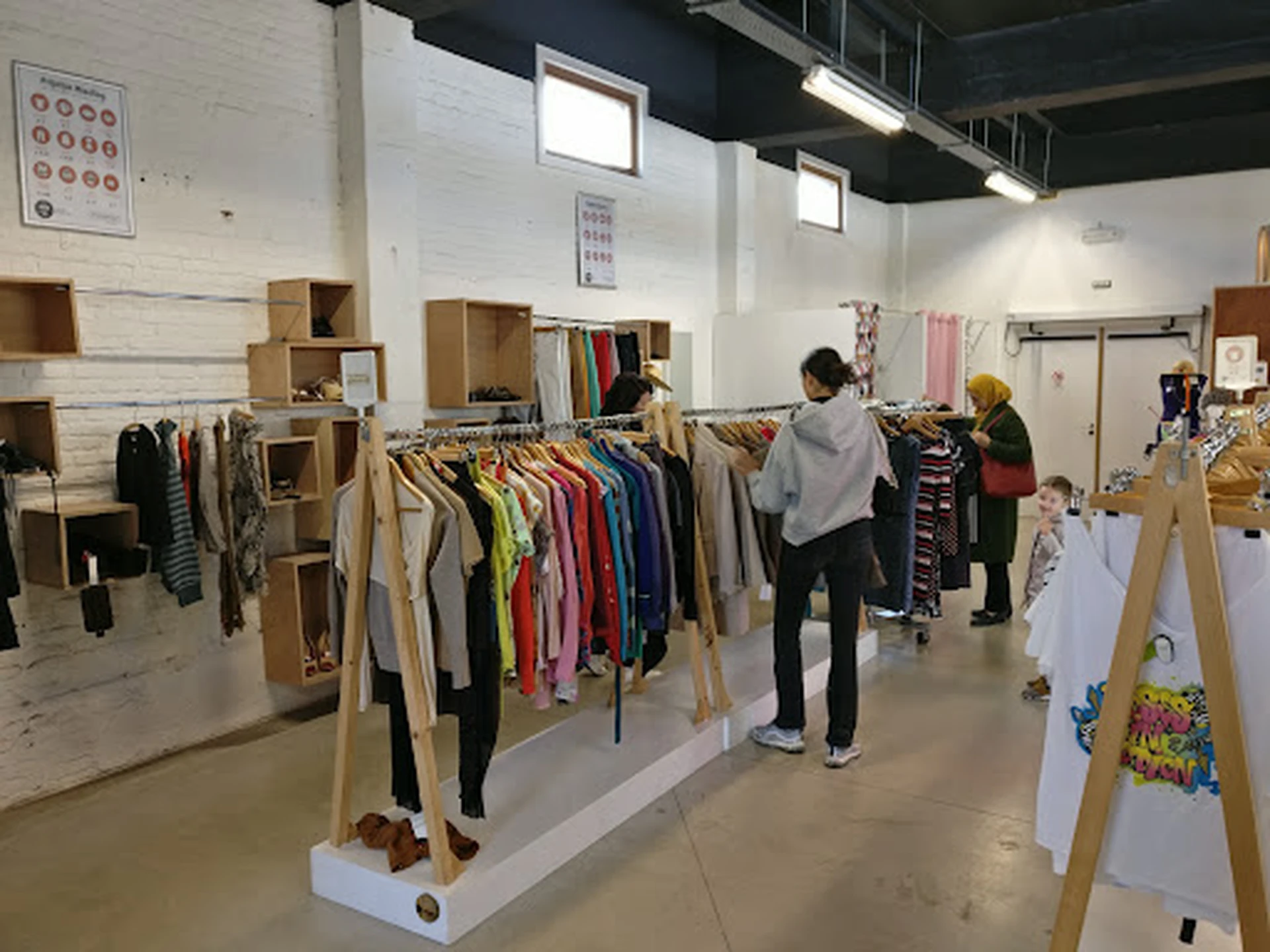 Winkelvloer met houten kledingrekken vol tweedehands kleding, enkele bezoekers aan het winkelen